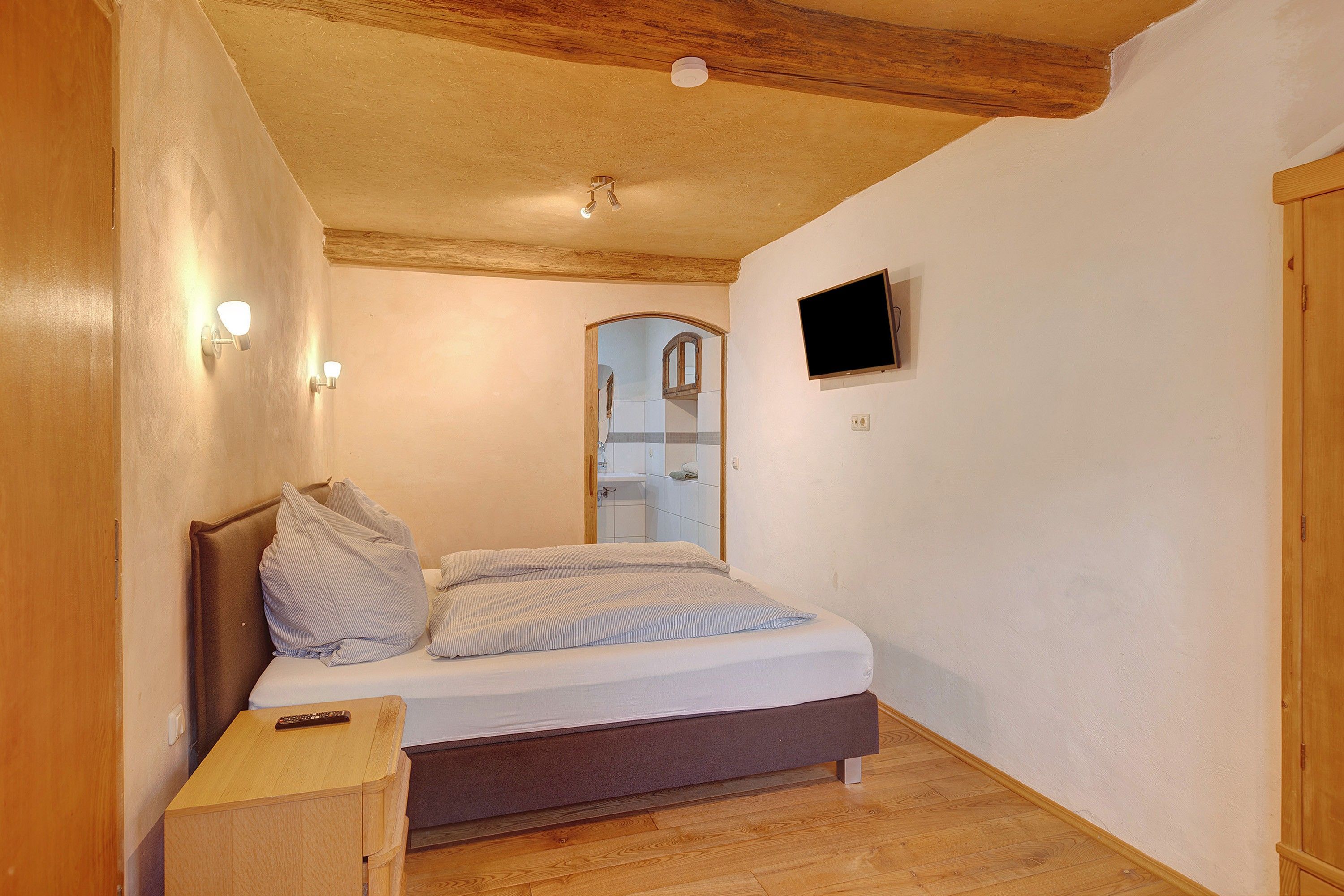 Une chambre à coucher avec un lit, une table de chevet et un téléviseur fixé au mur.