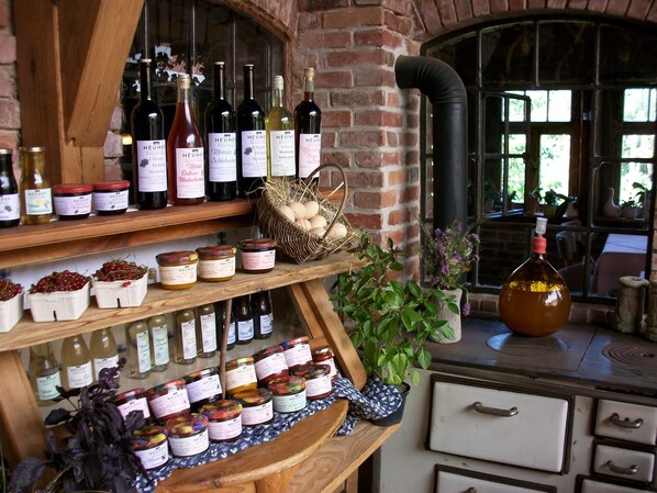 Une étagère en bois avec des bouteilles de vin, des pots de confitures et un panier d’œufs.