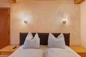 Une chambre avec deux lits, une porte en bois et une table de chevet avec une télécommande.