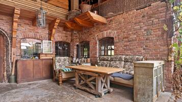 Un interior rústico con paredes de ladrillo visto, vigas de madera, una mesa de madera y un sofá con tapicería floral.