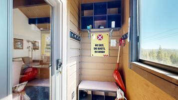 A compact room with a bench, a window, and a sign prohibiting skis and ski boots.
