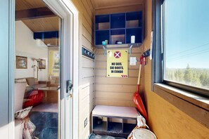 A compact room with a bench, a window, and a sign prohibiting skis and ski boots.