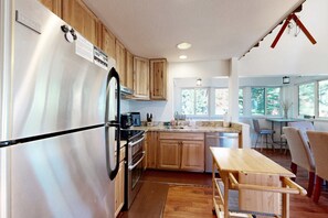 A kitchen with wooden cabinets, a stainless steel refrigerator, a wooden table, and a window providing natural light.