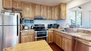 Cucina con mobili in legno, elettrodomestici in acciaio inossidabile, piano di lavoro in granito e una finestra che lascia entrare luce naturale.