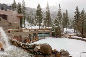 A building with a stone facade, a water feature, and a snow-covered landscape with trees. - Everline Resort & Spa - two units, Ski-in-ski-out, pools, gym, & ice rink (Olympic Valley)