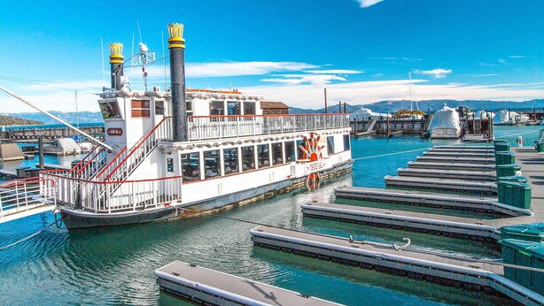 Una nave da fiume ormeggiata in una marina, con cielo sereno, acque calme e montagne sullo sfondo.