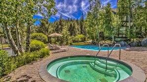 Una piscina con idromassaggio, circondata da alberi e lettini.