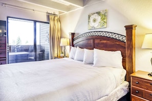 A hotel room with a large bed, a wooden headboard, a nightstand with a lamp, a sliding glass door, and a painting on the wall. - Experience Laid-back Mountain Living at this Townhome w Beach, Pool and Spa (South Lake Tahoe)