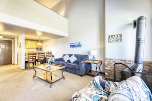 A living room with a sofa, coffee table, and fireplace. There is a kitchen area with wooden cabinets and a dining table. A painting is on the wall, and a sign reads 'LAKE HOUSE'. - Experience Laid-back Mountain Living at this Townhome w Beach, Pool and Spa (South Lake Tahoe)