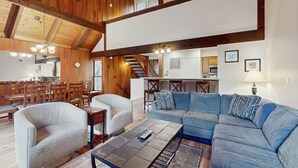 A spacious living area with a high ceiling, wooden beams, a blue sofa, and a dining area with wooden furniture. - Charming townhome with airy living space, amazing amenities, & near the beach (South Lake Tahoe)