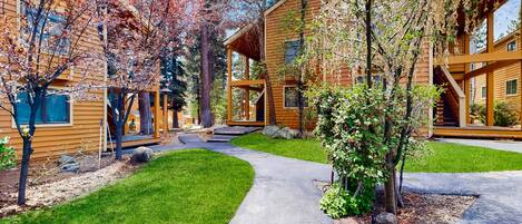 A modern log cabin with a covered porch, a stone pathway, and a well-maintained lawn.