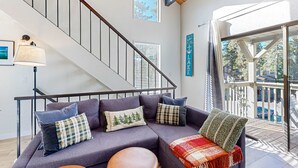 Ein modernes Wohnzimmer mit Treppe, einer Couch mit vielen Kissen, einer Lampe und Blick ins Freie.