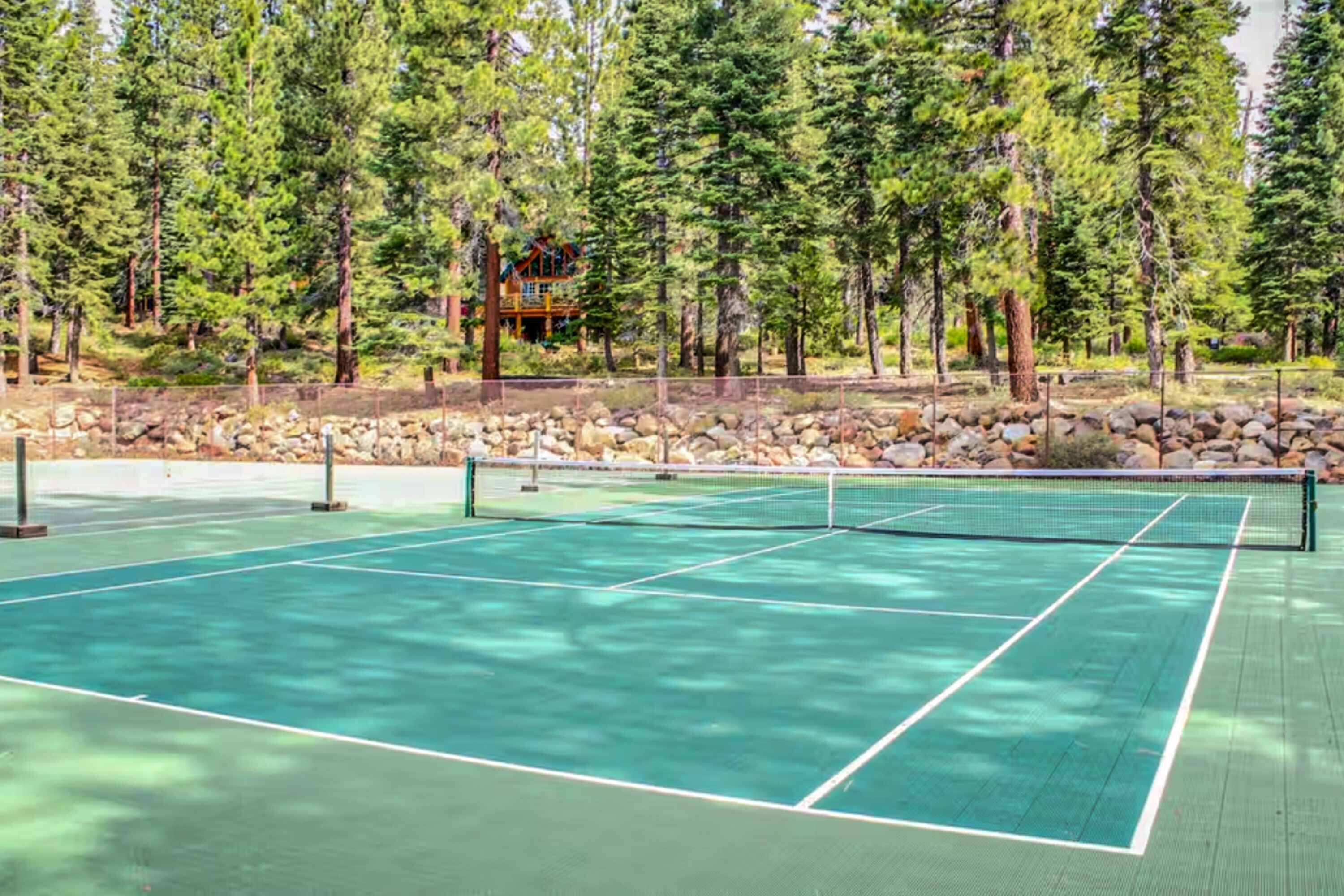 A tennis court surrounded by trees and a building in the background.