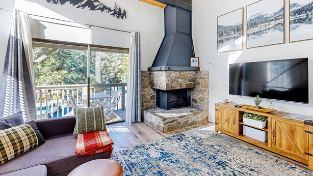 Ein Wohnzimmer mit Kamin aus Stein, einem großen Fernseher und einem Balkon mit Gartenmöbeln.