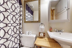 Une salle de bain comprenant des toilettes, un lavabo, un miroir et un rideau de douche à motifs géométriques.