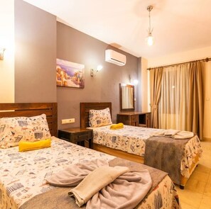 Ein Hotelzimmer mit zwei Betten, einem Bild an der Wand, einer Klimaanlage, einem Spiegel und einem Fenster mit Vorhängen.