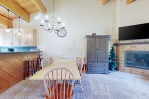 Ein Essbereich mit Holztisch und Stühlen, einer Pendelleuchte, einer Uhr, einem Fernseher und einem Kamin.