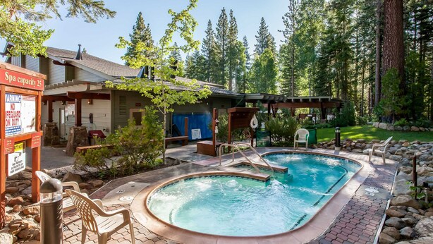 Un área de piscina con un letrero de capacidad para el spa, una zona de estar cubierta y un edificio con puerta azul.