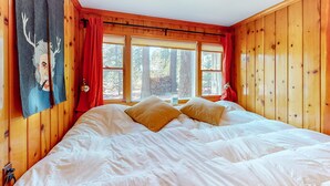 Quarto com painéis de madeira, uma cama grande, cortinas vermelhas e uma janela com vista para árvores.