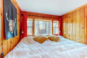 Ein Zimmer mit Holzwänden, einem großen Bett, roten Vorhängen und einem Fenster mit Blick auf Bäume.