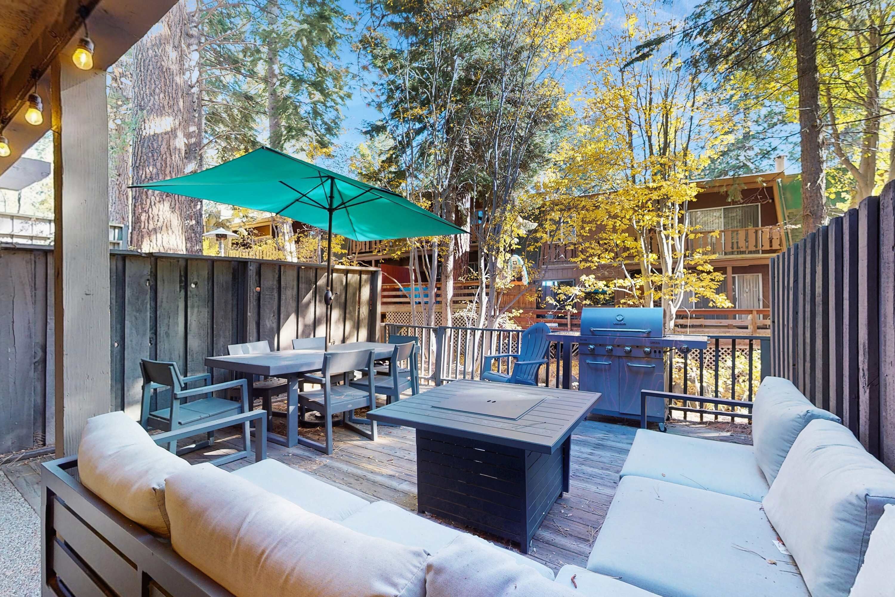 An outdoor patio with a wooden deck, a green umbrella, a barbecue grill, and outdoor furniture.