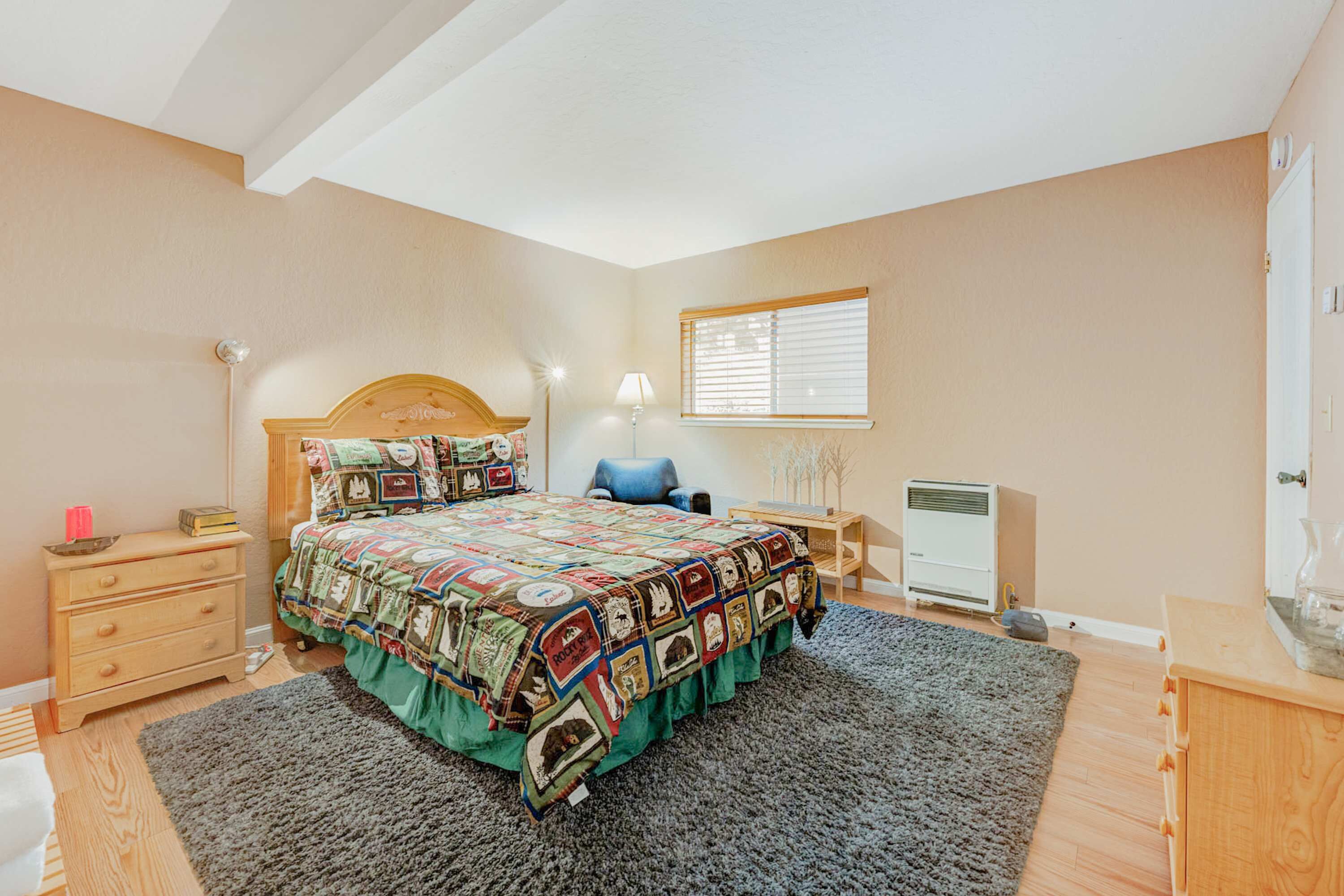 Un dormitorio con cama, mesitas de noche, escritorio, lámpara, radiador y ventana con persianas.