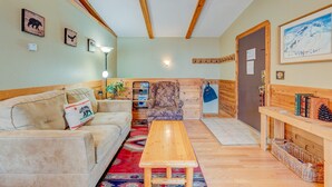Una sala de estar acogedora con un sofá, una mesa de madera, un sillón estampado y una puerta con perchero.