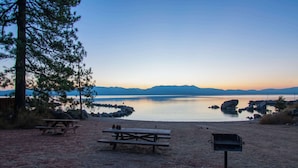 En picknickplats vid sjön med picknickbord och en grill.