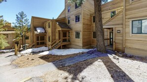 Un edificio de madera de varios pisos con una escalera que conduce a la entrada, un árbol en frente y el suelo cubierto de nieve.