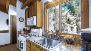 Una cocina con estufa, microondas, lavaplatos y ventana con vistas a un edificio.