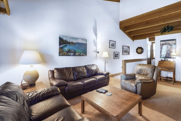 Una sala de estar con sofá, sillón y mesa de centro, un cuadro en la pared y una lámpara.
