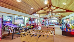 Un salón de juegos interior con vigas de madera en el techo, diversas máquinas de juego y una mesa de fútbol de mesa.