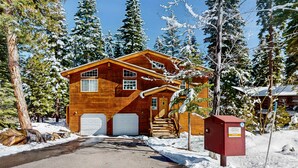Una baita di legno con due cancelli da garage, circondata da alberi innevati.