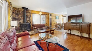Una sala de estar con sofá, mesa de centro de vidrio, chimenea, comedor y cocina con armarios.