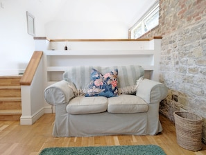 Una sala de estar con sofá, alfombra verde, escalera de madera y pared de piedra.