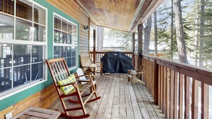 Una terrazza in legno con tettoia, sedie a dondolo e un barbecue.