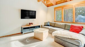 A modern living room with a sofa, ottoman, and a glass coffee table. - Ski-in/ski-out townhome with fireplace, pool, hot tub & on-site ski/sled hill (Tahoe City)
