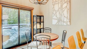 A dining area with a round table, chairs, a chandelier, a bookshelf, and a large abstract painting on the wall. - Ski-in/ski-out townhome with fireplace, pool, hot tub & on-site ski/sled hill (Tahoe City)