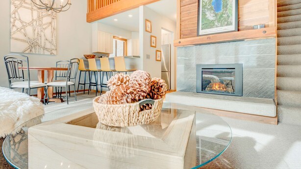 A modern living room with a glass coffee table, a fireplace, a dining area with chairs, and a large abstract painting on the wall. - Ski-in/ski-out townhome with fireplace, pool, hot tub & on-site ski/sled hill (Tahoe City)