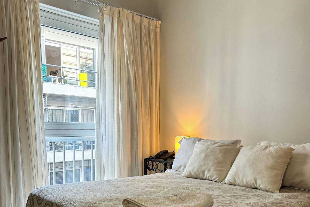 A hotel room with a bed, curtains, a bedside lamp, and a view of a balcony.