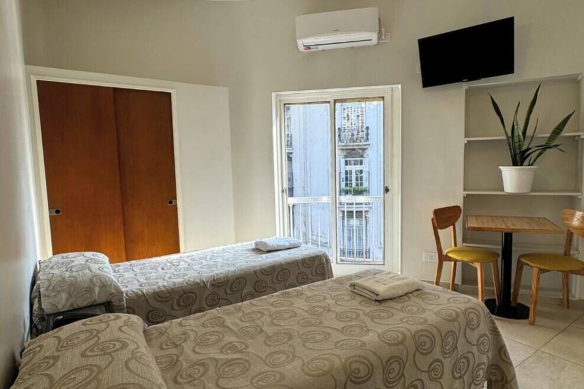 A hotel room with two beds, a TV, a potted plant, and a balcony with a view.