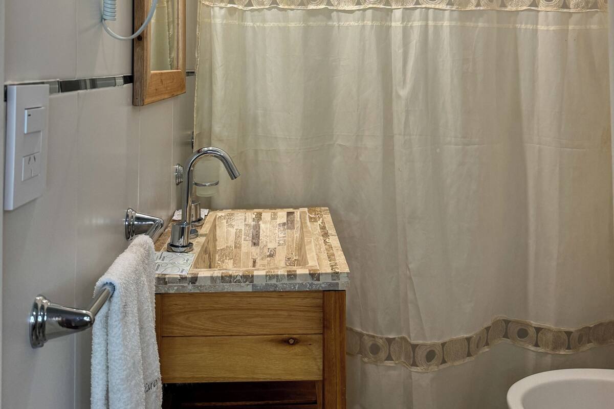 A bathroom with a shower curtain, a sink with a wooden vanity, a mirror, and a hairdryer mounted on the wall.