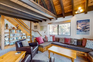 A cozy living area with a wooden staircase, a bookshelf, a sofa set, and a large window.