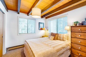 A bedroom with a bed, wooden dresser, windows, and a ceiling fan.