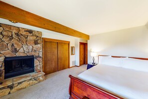 A bedroom with a stone fireplace, wooden ceiling beams, a bed, and a door. - Fantastic lakefront condo with tennis, skiing, fireplace, & W&D, sleeps 6 (Zephyr Cove)