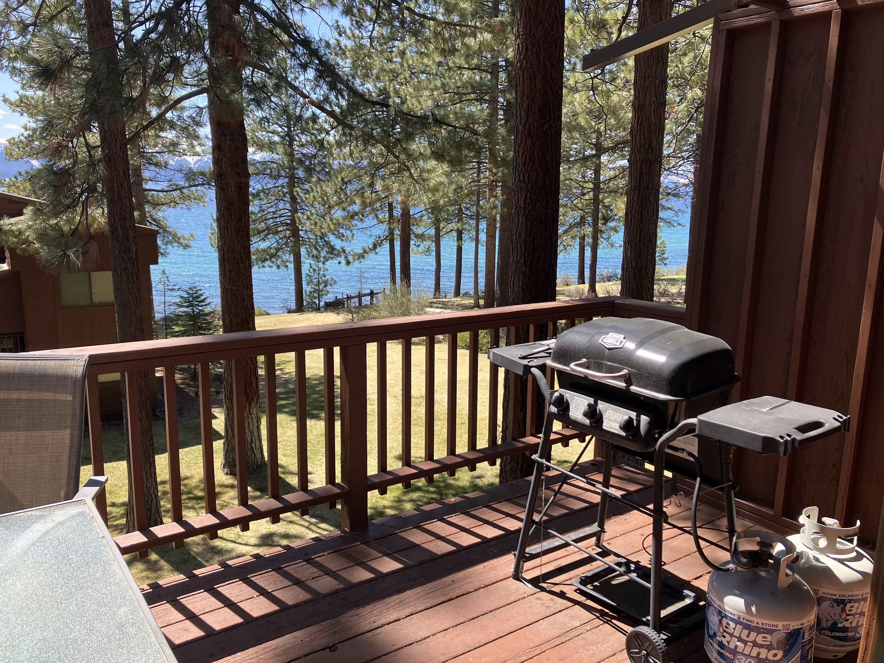 A deck with a grill and propane tanks, overlooking a lake with trees.