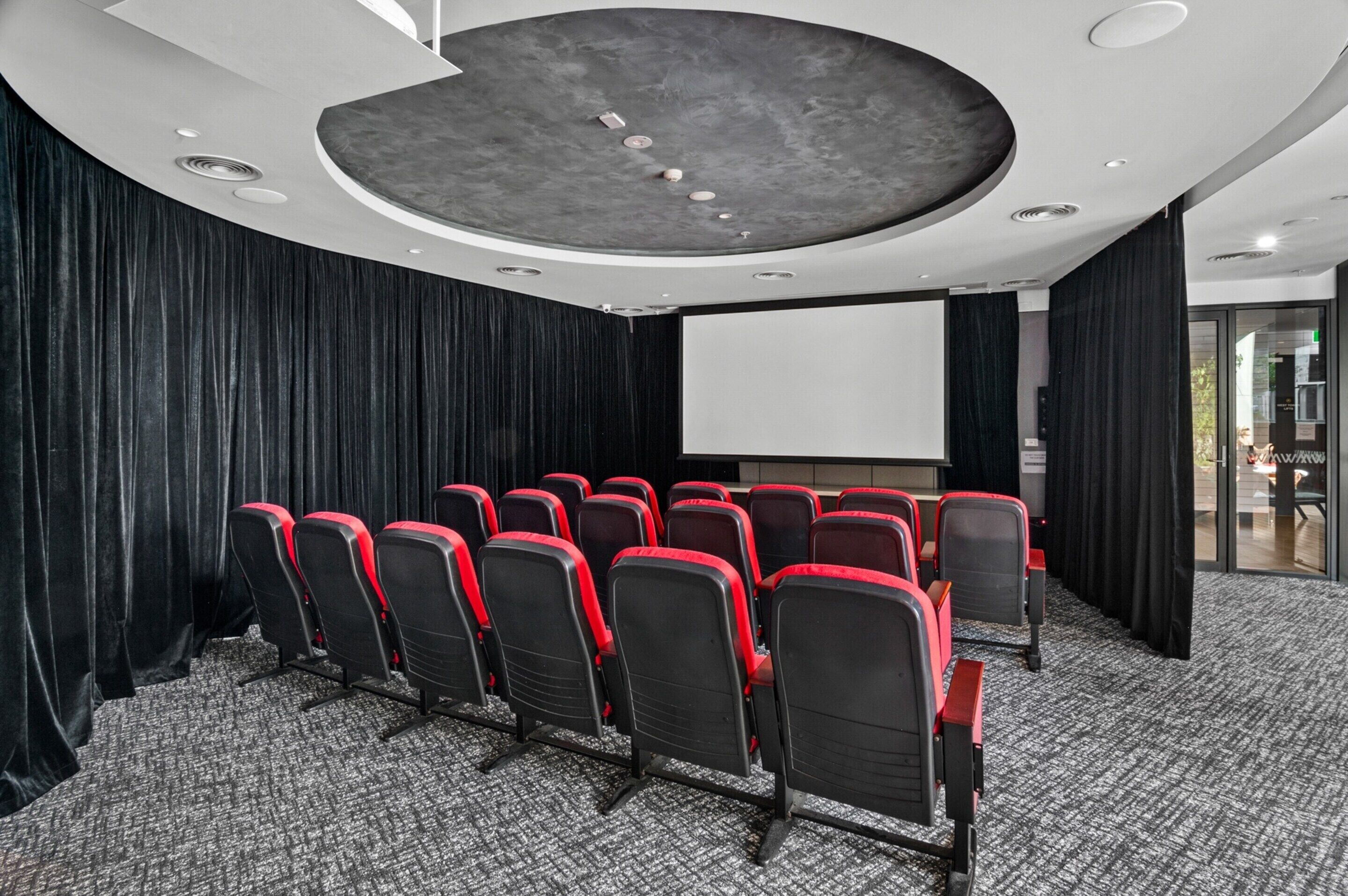 A conference room with a large screen, rows of chairs, and a modern ceiling design.
