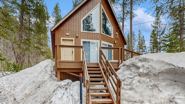 A cabin with a wooden exterior, a large window, and a staircase leading up to the entrance. - Cozy, dog-friendly getaway with wood stove & washer&dryer (Soda Springs)