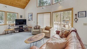 A spacious living room with a high ceiling, large windows, a television, a sofa, and a coffee table. - Cozy, dog-friendly getaway with wood stove & washer&dryer (Soda Springs)