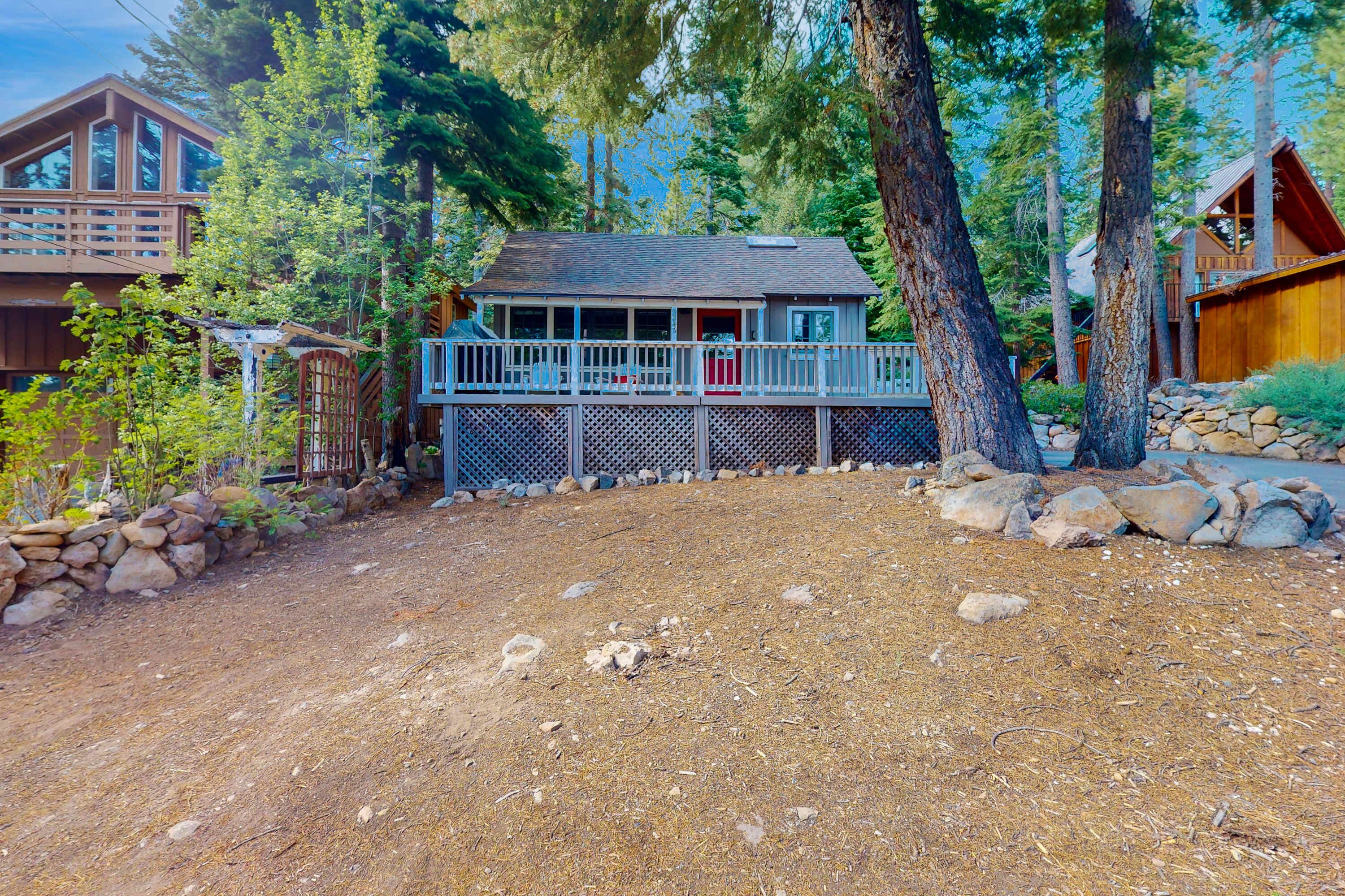 A cabin with a wooden deck, surrounded by trees and a stone wall.